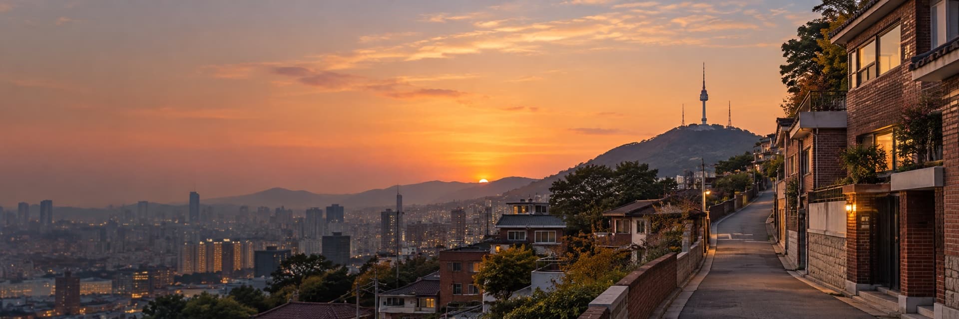 A hillside residential street in Seoul at sunset, with brick villas and N Seoul Tower in the distance