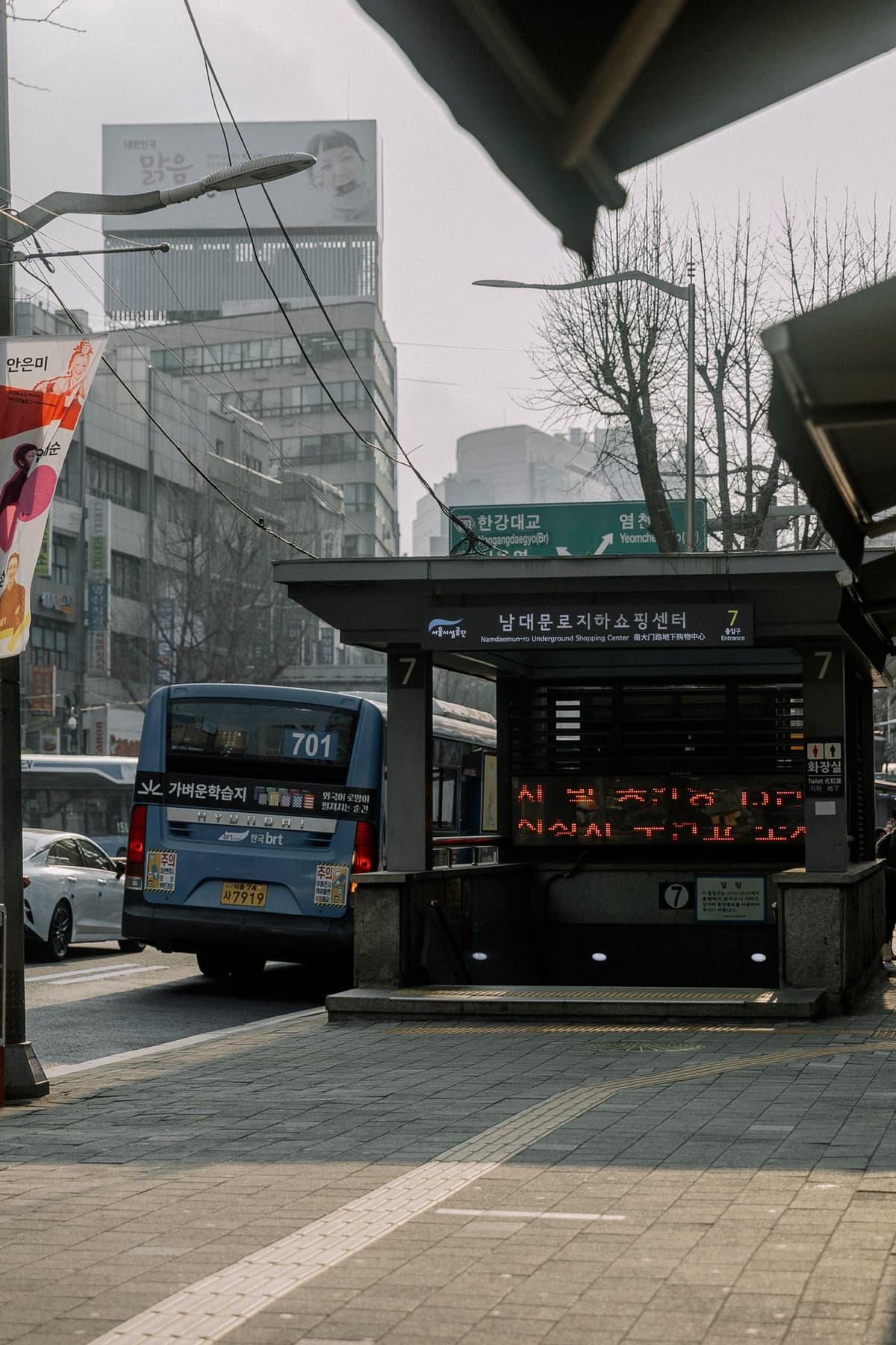 남대문로 지하쇼핑센터 7번 출입구 옆 도로에 파란 버스가 서 있다.